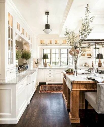 Cuisine lumineuse style ferme moderne avec armoires blanches, comptoirs en marbre, îlot en bois rustique et plancher foncé.